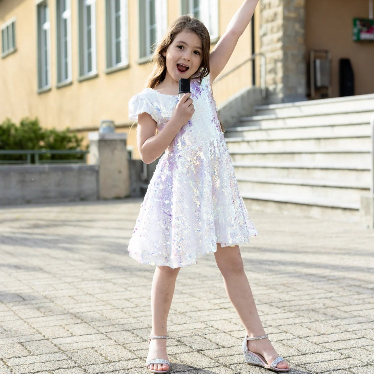 Young girl in a white dress standing on a paved area with a building in the background